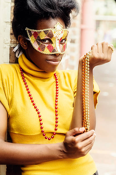 Young Woman in Mask With Beads A young african american woman outdoors wearing a mask and Mardi Gras beads. mardi gras women stock pictures, royalty-free photos & images