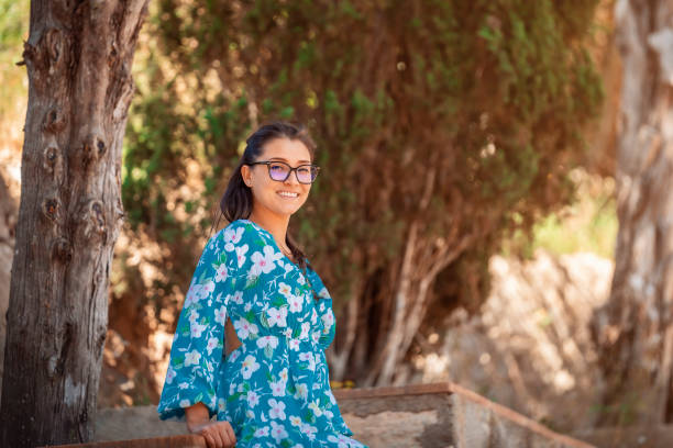 young woman in summer dress and glasses standing on stairs looking at the camera stock photo