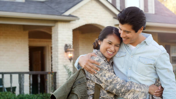 Young woman in uniform hugs a young man tightly while smiling A young woman in uniform rests her head on a young man as they share a heartfelt hug in front of a home. veterans returning home stock pictures, royalty-free photos & images