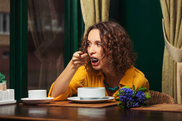 Young woman in yellow shirt eating a soup at restaurant stock photo