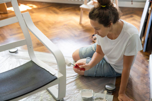 Young woman is coloring a chair at home Young woman painting a black wooden chair in white. DIY project concept upcycling stock pictures, royalty-free photos & images