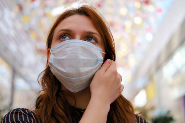A young woman is considering whether to remove the medical mask after the end of the quarantine due to the coronavirus. Portrait of a girl after the flu virus epidemic, close-up A young woman is considering whether to remove the medical mask after the end of the quarantine due to the coronavirus. Portrait of a girl after the flu virus epidemic, close-up surgical mask stock pictures, royalty-free photos & images