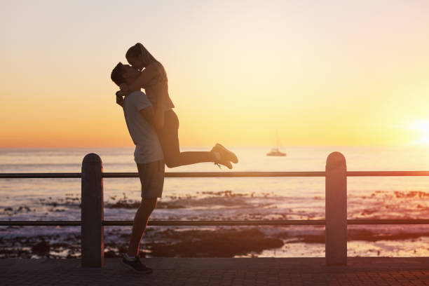 giovane donna salta tra le braccia del fidanzato e gli dà un bacio al tramonto - couple kiss foto e immagini stock