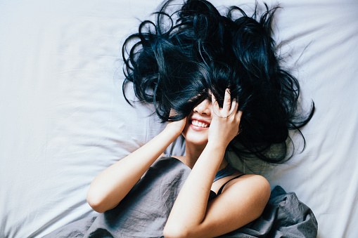 Happy young woman laughing in bed, hair covering the face.