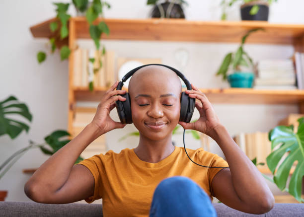 A young woman listens to music with headphones on the sofa in the living room stock photo