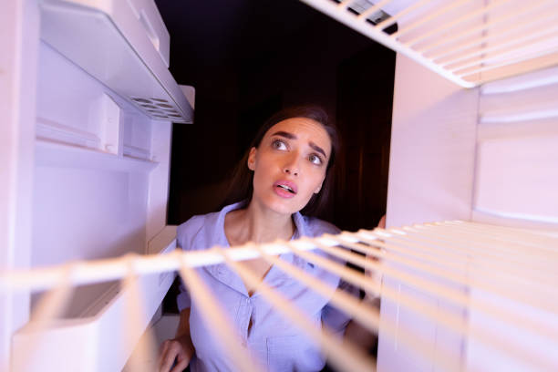 彼女の冷蔵庫の空の棚を見ている若い女性 - 冷蔵庫　中 ストックフォトと画像