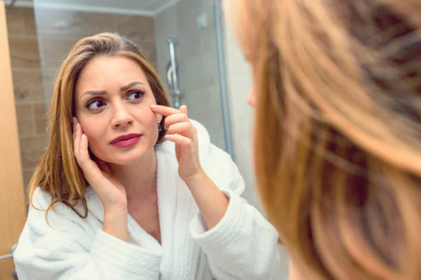 Mujer joven en espejo en baño preocupado por acné y envejecimiento - foto de stock