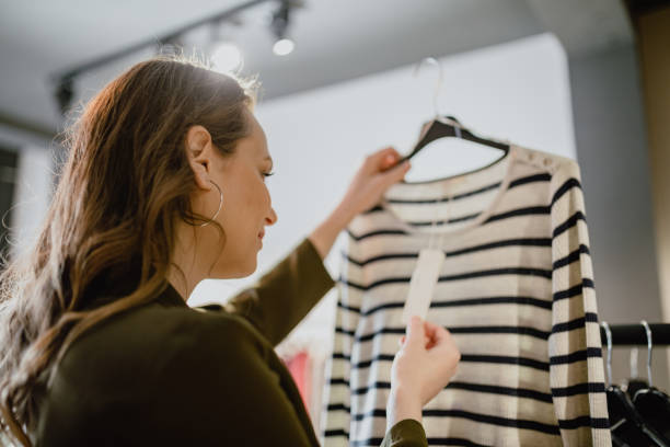 Young woman looking in to price tag in the clothing store stock photo