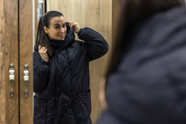A young woman looks at herself in a closet mirror. A young woman in a black jacket looks at herself in the mirror of a closet in the hallway. marie kondo stock pictures, royalty-free photos & images