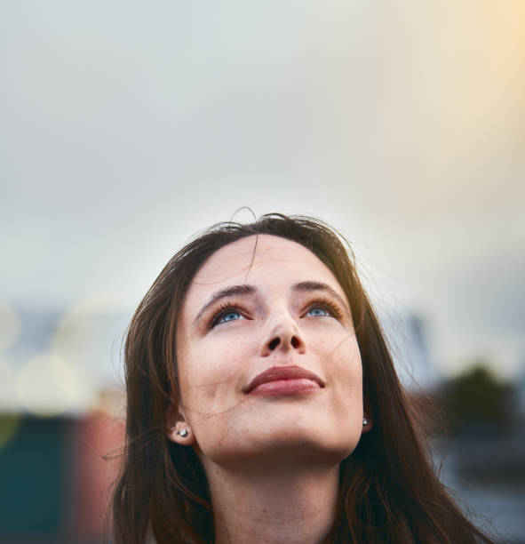 unga kvinnan ser hoppfull som hon höjer ögonen mot himlen - föreställningsförmåga bildbanksfoton och bilder