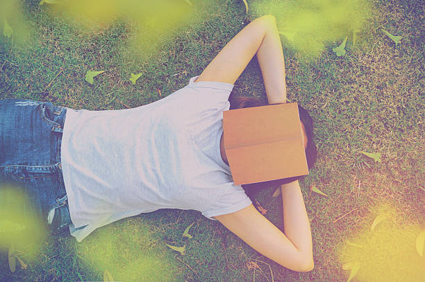 young woman lying on a lawn with a book. stock photo