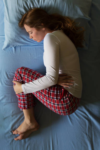 giovane donna sdraiata sul letto nel dolore, pm, mestruazioni, sensazione di malessere e depressa - kostic foto e immagini stock