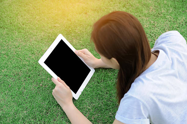 Young woman lying on grass using tablet stock photo