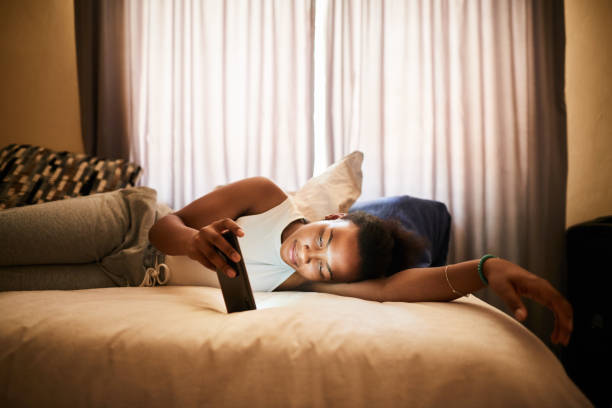 Young woman lying on her bed watching something on her cellphone stock photo
