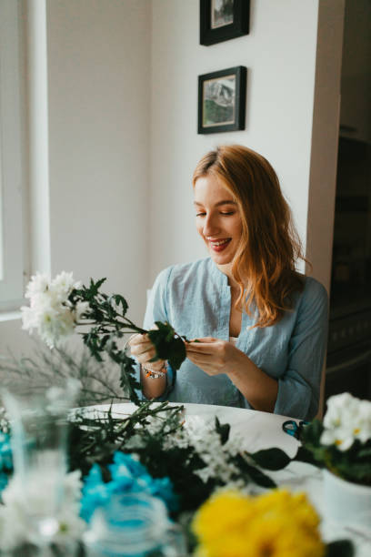 Young woman making flower arrangements at home stock photo