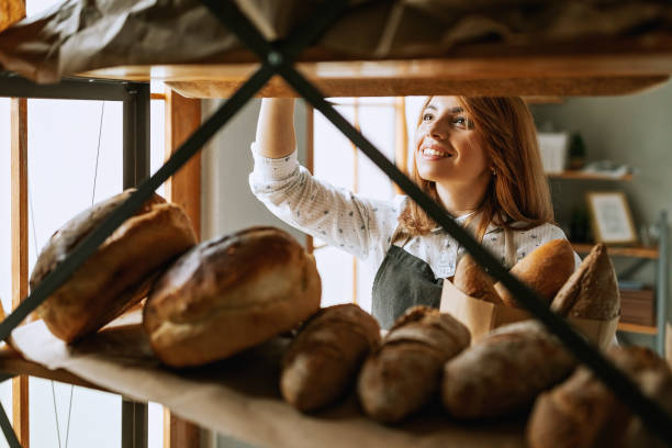 молодая женщина товар хлеб в магазине - пекарь стоковые фото и изображения