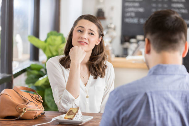 Young woman on a bad blind date Young woman makes an uneasy or disinterested face while on a blind date in a coffee shop. The back of the young man's head is seen in the foreground. bad date stock pictures, royalty-free photos & images