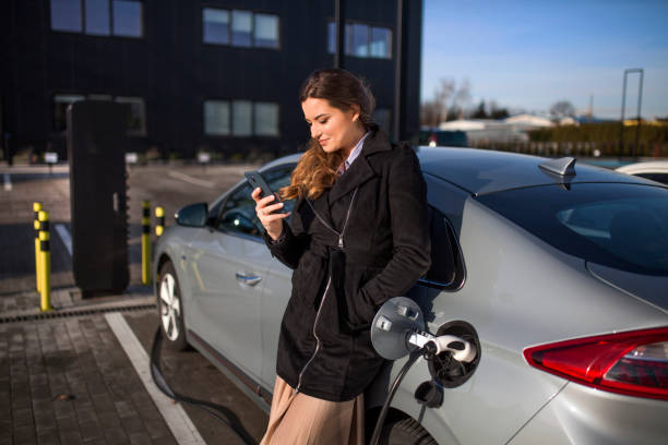 Young woman on a parking lot, charging her electric car stock photo