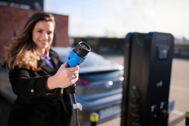 Young woman on a parking lot, holding a car charger plug stock photo