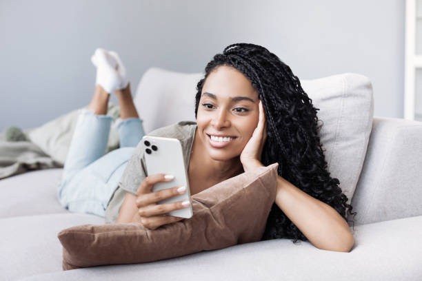Young woman on sofa looking at smartphone, relaxing at home stock photo