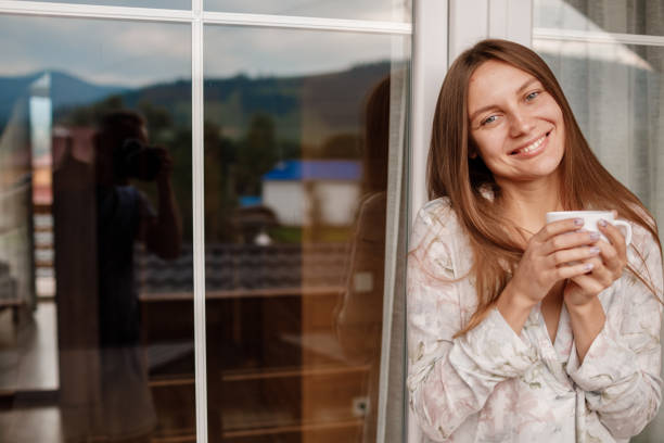 Young woman on the balcony holding a cup of coffee or tea in the morning. She in hotel room looking at the nature in sumer. Girl is dressed in stylish nightwear. Relax time. Young woman on the balcony holding a cup of coffee or tea in the morning. She in hotel room looking at the nature in sumer. Girl is dressed in stylish nightwear. Relax time pyjama moulant homme stock pictures, royalty-free photos & images