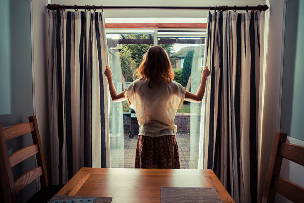 Young woman opening the curtains at sunrise stock photo