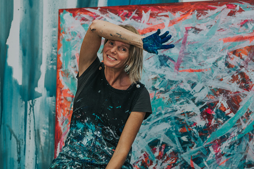 Young woman paints an abstract picture with her hands in her interior studio