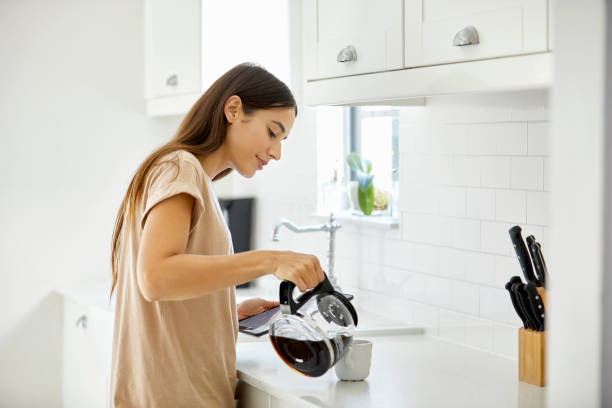 jonge vrouw koffie in beker thuis gieten - woman drinking coffee stockfoto's en -beelden