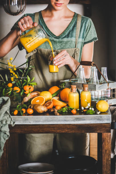 young woman pouring fruit immune boosting drink to bottle - boosting imagens e fotografias de stock