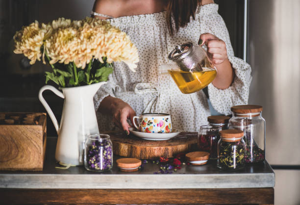 jonge vrouw gieten groene thee van pot in beker - thee stockfoto's en -beelden