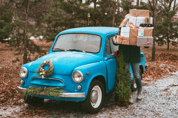 young woman preparing holiday xmas gifts Decorated with blue retro car with festive Christmas tree branches stock photo