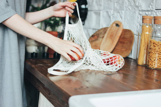 Young woman pulls apples out of knitted rag bag string bag shopper in kitchen, zero waste, slow life stock photo