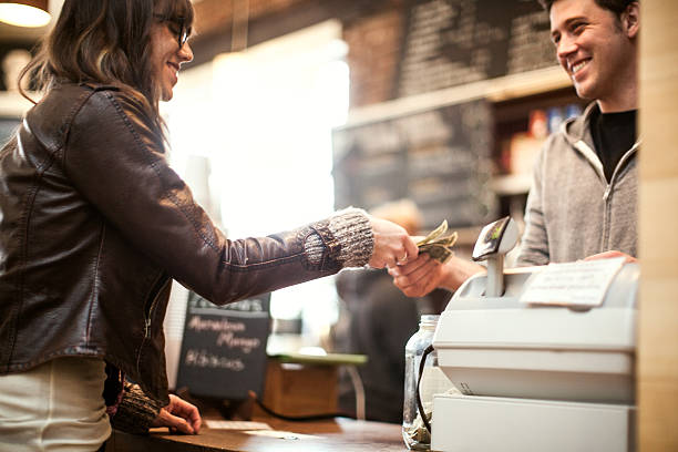 Young woman purchasing coffee A woman is paying at a coffee shop.  The cashier is a young man.  They are smiling at each other. paper currency stock pictures, royalty-free photos & images