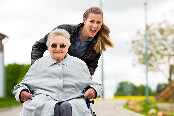 young woman pushing old woman in wheelchair - huismeester stockfoto's en -beelden