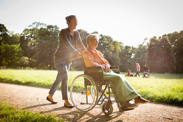 young woman pushing senior lady in wheelchair through a park stock photo