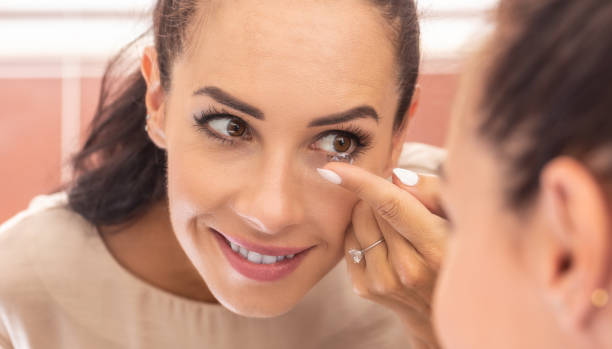 A young woman puts contact lenses in her eyes in the morning in the bathroom in front of a mirror. stock photo