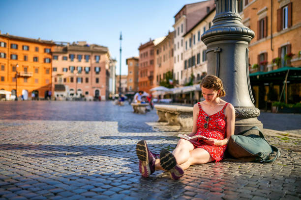 A young woman reads a book in the quiet of Piazza Navona in the baroque heart of Rome stock photo
