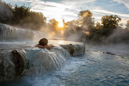 Young woman relaxing at natural spa with waterfalls and hot springs at Saturnia thermal baths