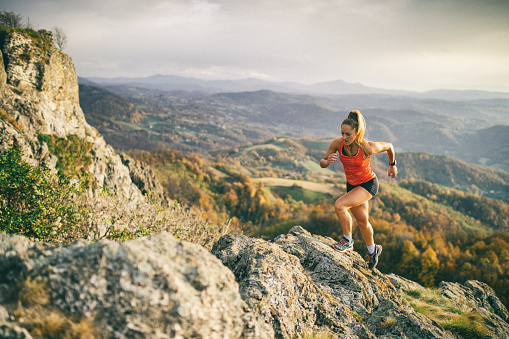 Action photo of athlete woman trail runner running and climbing over mountain cliff. Extreme terrain and beautiful light before sunset after rain.