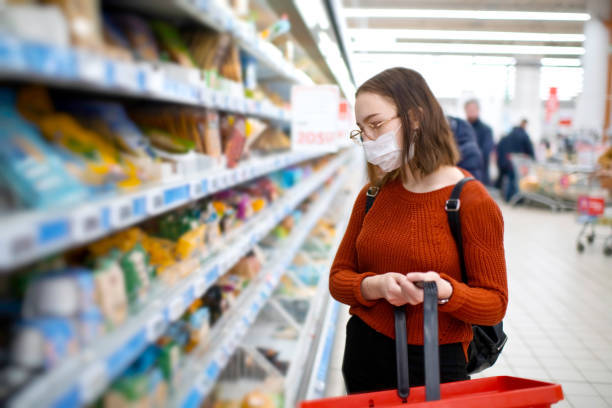식료품점에서 쇼핑하고 보호 용 마스크를 착용한 젊은 여성 - 시장 소매점 뉴스 사진 이미지