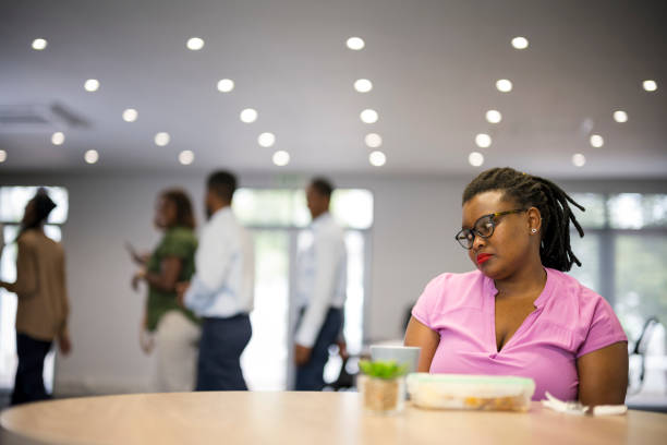 Young woman sits alone while coworkers go out to lunch together stock photo
