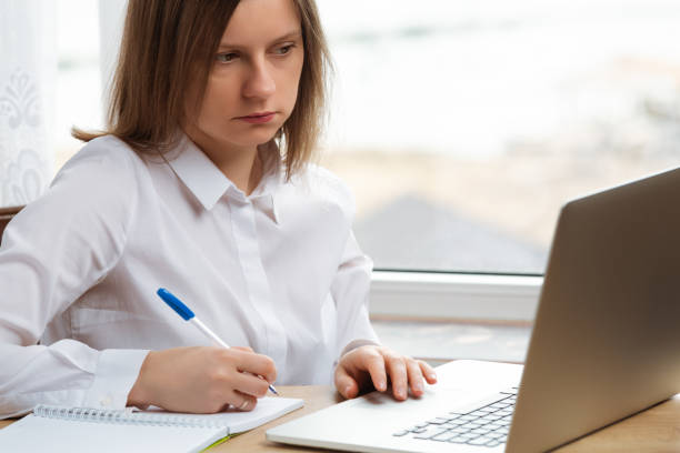 Young woman sitting at working table with laptop and notepad to do work from home. stock photo