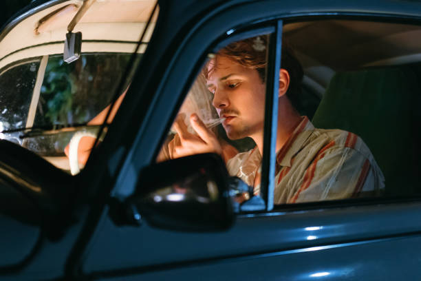 jeune femme assise à côté d’un homme fumant du joint de marijuana dans une voiture - cannabis voiture jeune photos et images de collection