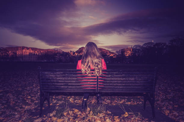 Young woman sitting facing away on a park bench stock photo