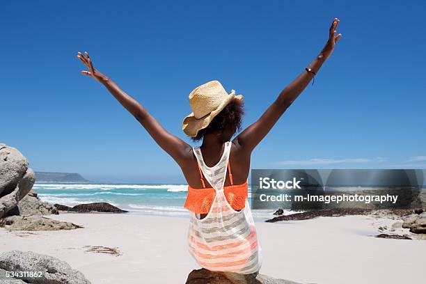 Young woman sitting on beach with her hands outstretched