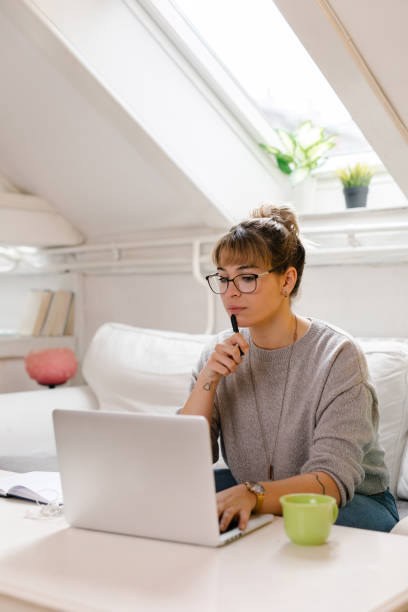 Young woman sitting on sofa and using laptop for studying stock photo