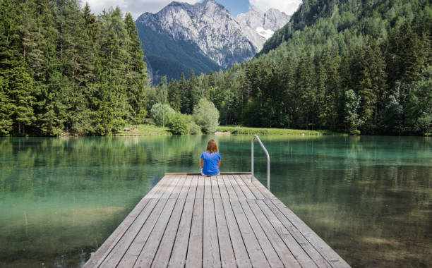 Young woman sitting on wooden footbridge in scenic mountain lake plansarsko, slovenia stock photo