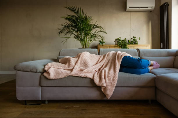 Young woman sleeping under blanket Young woman lying down on sofa in living room covered by blanket. Unrecognizable person. headache stock pictures, royalty-free photos & images