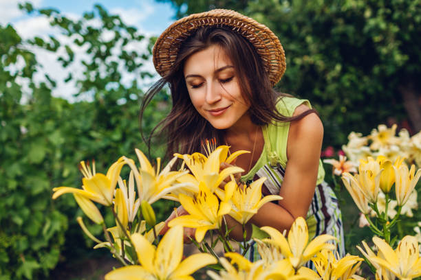 Young woman smelling flowers in garden. Gardener taking care of lilies. Gardening concept stock photo
