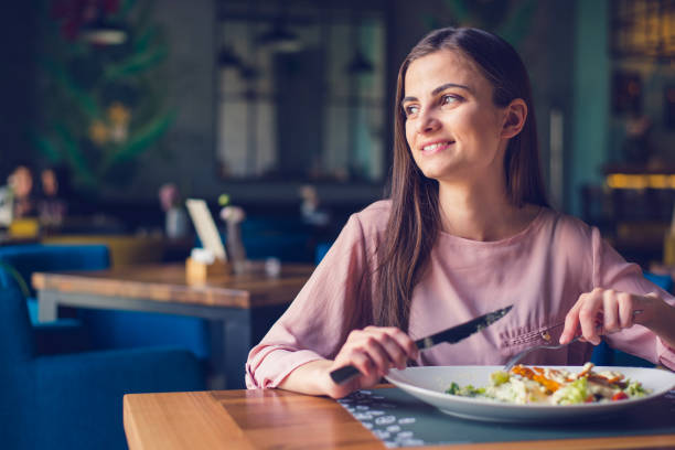 Young woman smiling and looking away while eating lunch stock photo